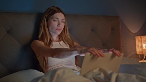 ダークアパートのベッドルームでノートパソコンを閉じているスリープレスの女性が閉じます. 疲れたオンラインワーカーは,ベッドタイムに居心地の良いベッドに座ってリモートワークを終了します. 魅力的な深刻な女性は夜の家で過労睡眠を感じる. - 映像、動画
