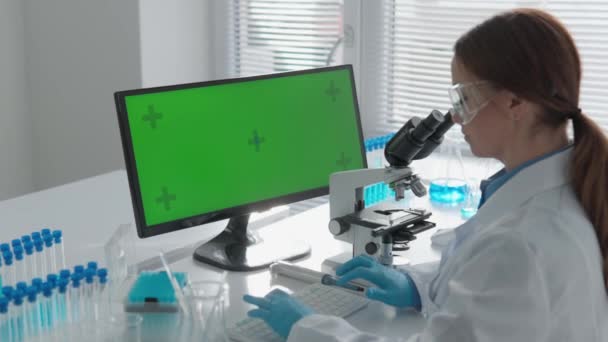 Chroma sleutel groen scherm. Een laboratorium waar de wetenschapper onderzoek doet op het gebied van geneeskunde en chemie. Met behulp van een microscoop bestudeert hij biologische structuren, en met behulp van een computer, - Video