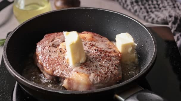 Un chef agrega mantequilla, romero y ajo a una sartén de carne de res en la cocina. El proceso de cocinar un delicioso bistec, primer plano de la comida - Metraje, vídeo