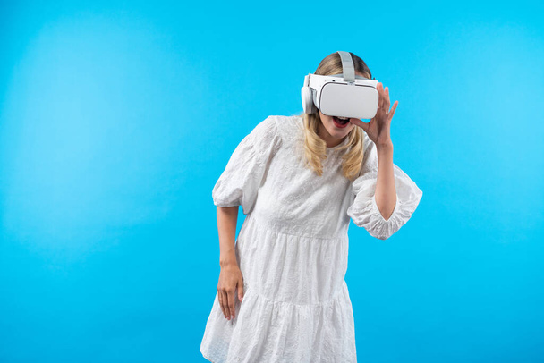 Fille avec lunettes VR regardant autour du monde de l'hologramme. Femme surprise de connecter métaverse en utilisant le monde de la réalité visuelle et debout à fond bleu. Concept de technologie d'innovation. Machines et appareils. - Photo, image