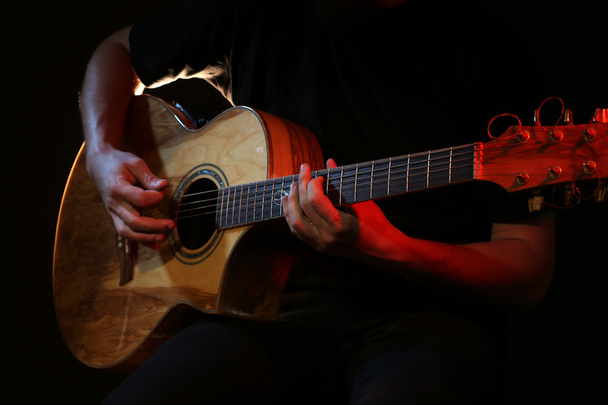 Young man playing on acoustic guitar on dark background - Fotografie, Obrázek