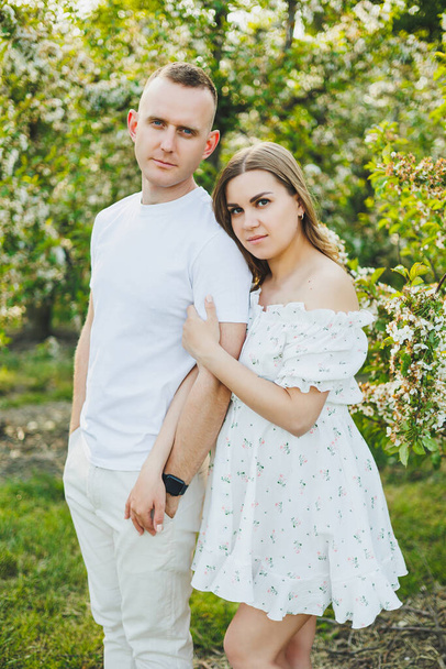 Beautiful young couple in spring garden. Beauty lifestyle family concept. A happy mother is expecting a baby. A happy young couple in a blooming garden - Photo, Image