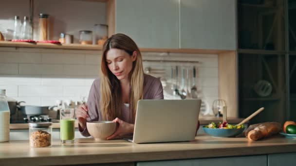 Ontbijt vrouw op zoek laptop scherm op moderne keuken. Ontspannen meisje eet alleen eten en geniet van de film op de computer. Aantrekkelijke jonge zakenvrouw lezen e-mail rapport vroege ochtend voor het werk. - Video