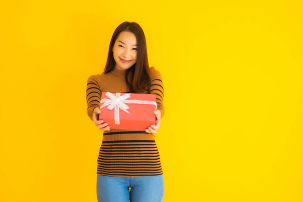 Muotokuva kaunis nuori aasialainen nainen onnellinen hymy punainen lahja laatikko keltainen eristetty tausta
 - Valokuva, kuva
