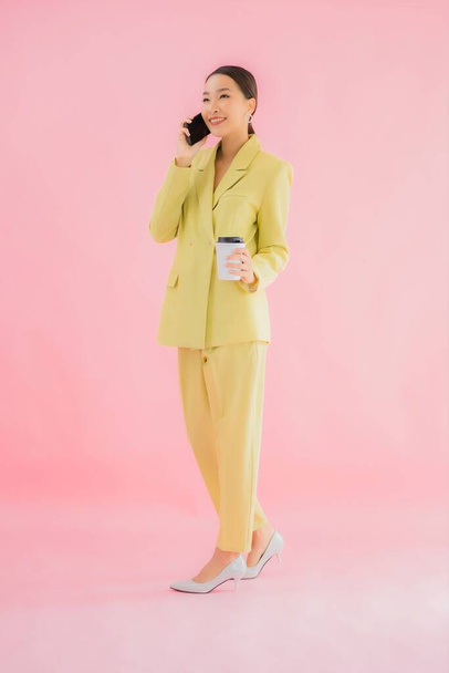 Portret mooie jonge aziatische zakenvrouw gebruik slimme mobiele telefoon met koffiebeker op kleur achtergrond - Foto, afbeelding