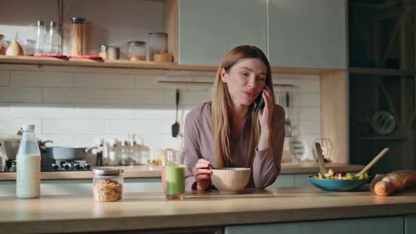 Ευτυχισμένη γυναίκα καλεί στον πάγκο της κουζίνας. Χαμογελαστό κορίτσι μιλάει smartphone το πρωινό Σαββατοκύριακο. Θετική κυρία απολαμβάνουν εγχώρια επικοινωνία από το κινητό τηλέφωνο. Χαριτωμένη νοικοκυρά μιλώντας στην κουζίνα. - Πλάνα, βίντεο