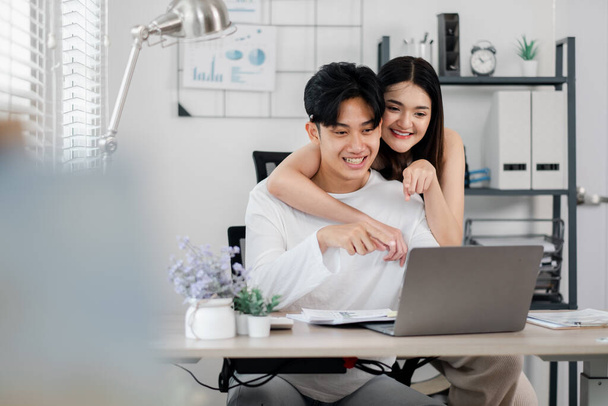 Jeune couple enthousiaste naviguant en ligne, pointant vers leur écran d'ordinateur portable avec excitation dans un élégant bureau à domicile. - Photo, image
