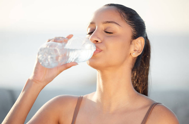 Woman, athlete and drinking water outdoors, thirsty and runner hydration after workout or cardio. Female person, detox and mineral liquid for recovery after exercise, fitness sports and nutrition. - Photo, Image