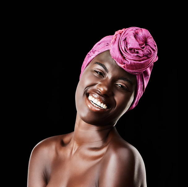 Zwarte vrouw, hoofddoek en schoonheidsportret met glimlach, huidverzorging en natuurlijke cosmetica in de studio. Traditionele, tulband en Afrikaanse mode met wellness en huidgloed met make-up en donkere achtergrond. - Foto, afbeelding