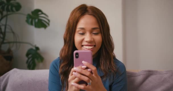 La donna latina scrive messaggi sul cellulare ridendo a casa. Felice ispanici tipi femminili su smartphone seduto sul divano. Tolleranza razziale mista - Filmati, video