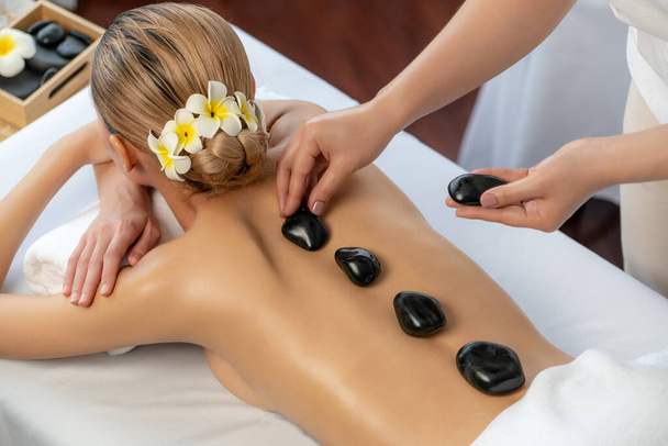 Hot-Stone-Massage im Wellness-Salon im Luxus-Resort mit Tageslicht Gelassenheit Ambiente, glückselige Kundin genießen Wellness-Basaltstein-Massage gleiten über den Körper mit wohltuender Wärme. Ruhige Lage - Foto, Bild