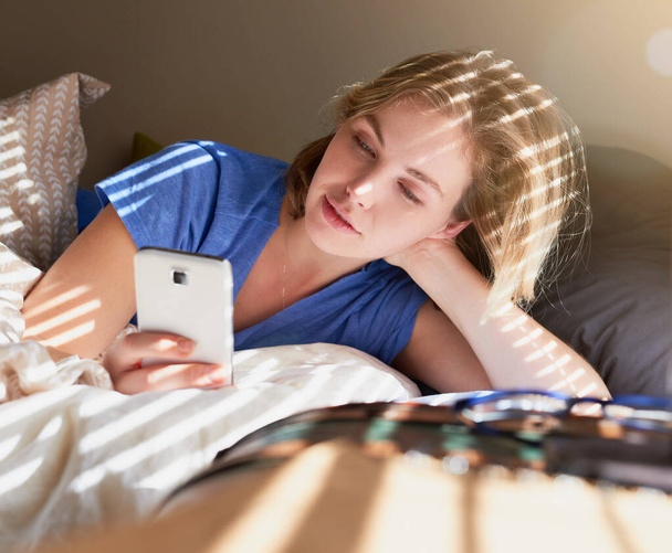 Woman, bed and relax with phone for search on social media, technology or video call in bedroom. Female person, mobile and scroll for news on digital in Europe, check with application for new story. - Photo, Image