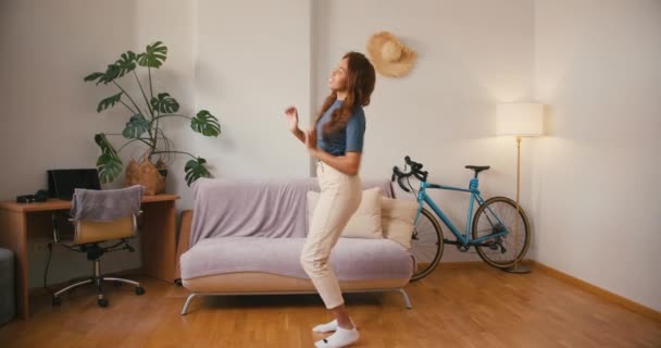 La joven latina baila sola en el apartamento. Bastante alegre mujer hispana se mueve escuchando música en la sala de estar. Tolerancia de raza mixta - Metraje, vídeo