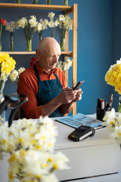 Starszy człowiek o jasnej skórze, sprzedawca kwiatów, organizuje dostawę kwiatów przez telefon. Bardzo duży wolumen dostawy - Zdjęcie, obraz