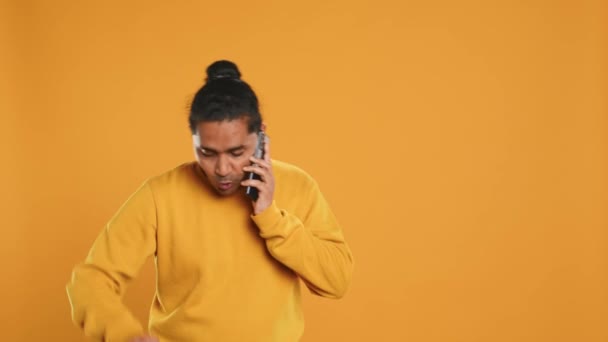 Delivery man arguing with customer on phone after arriving at destination and waiting for him, studio background. Indian person doing deliveries, scolding late client on telephone call, camera A - Footage, Video