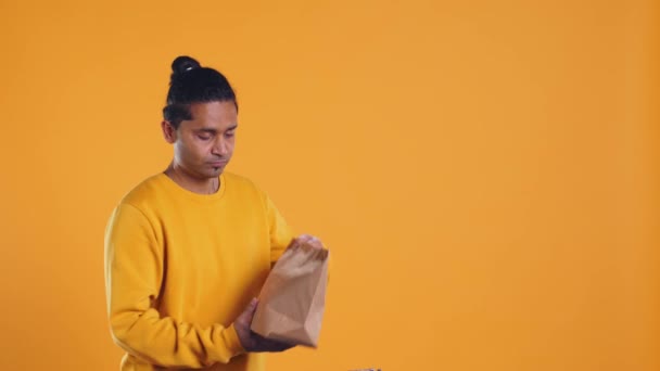 El repartidor de pizza indio recibe una orden de comida para llevar de la mochila térmica, dándosela al cliente que paga con tarjeta. Mensajero que ofrece bolsa de papel de almuerzo y punto de venta al cliente, fondo de estudio, cámara B - Imágenes, Vídeo