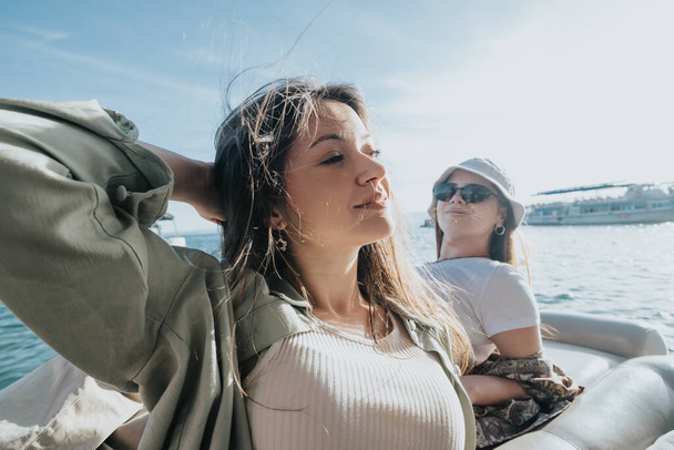 二人の若い女性が太陽を浴びて海で息をのむようなボートに乗り,カジュアルなシックでリラックスした様子を演出します.. - 写真・画像