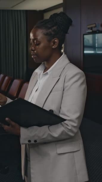 Empurre verticalmente o retrato de uma advogada afro-americana positiva em terno cinza posando com pasta de couro preto na luxuosa sala de conferências da firma de advocacia e olhando para a câmera - Filmagem, Vídeo