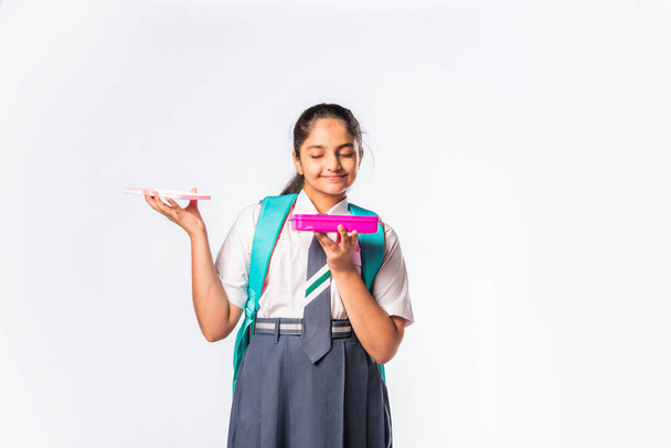 Happy Indian asian schoolgirl in school uniform holding a lunch box against white background - Photo, Image