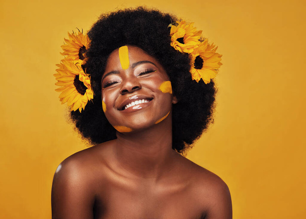 Zwarte vrouw, zonnebloem en verf in studio met make-up voor schoonheid met creatieve, zelfvertrouwen en lente. Cosmetica, gele achtergrond en eigenliefde met natuurlijk voor bloemengezicht met glimlach voor huidverzorging. - Foto, afbeelding