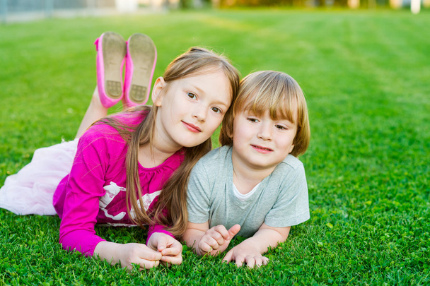 Outdoor portrait of two cute kids, laying on a bright green lawn at sunset - Photo, Image