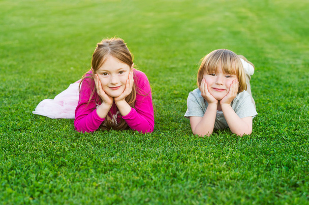 Portrait extérieur de deux mignons enfants, allongés sur une pelouse vert vif au coucher du soleil
 - Photo, image