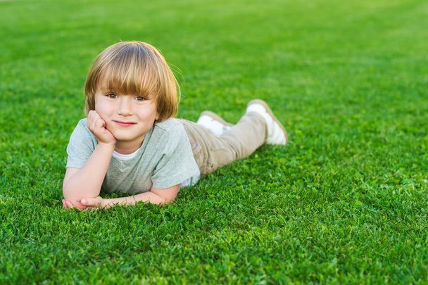 Retrato al aire libre de adorable niño rubio acostado en un césped verde fresco brillante
 - Foto, imagen