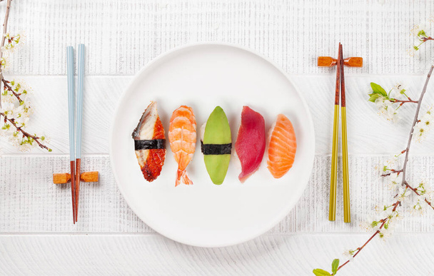 Talerz sushi na stole ozdobiony gałązką wiśni i pałeczkami, uosabiający japońską kulturę żywności - Zdjęcie, obraz