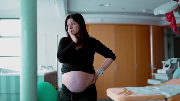 Mujer embarazada de 30 años preocupada de pie en la Clínica del Hospital, preparándose para el nacimiento. embarazada con expresión ansiosa a la espera del parto - Imágenes, Vídeo