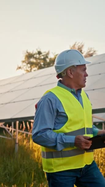 Alternative source of electricity. Inspector engineer man holding digital tablet working in solar panels power farm, photovoltaic cell park. Innovation and green power concept  - Felvétel, videó