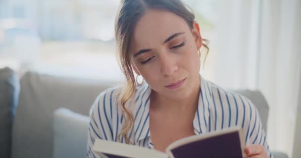 Una mujer enfocada y contemplativa absorta en leer un libro mientras está sentada en un sofá en la sala de estar, absorta en el mundo de la literatura - Metraje, vídeo