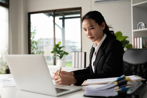 Сосредоточенная азиатская женщина-бухгалтер делает бумажную работу в офисе с плановыми документами на столе. - Фото, изображение