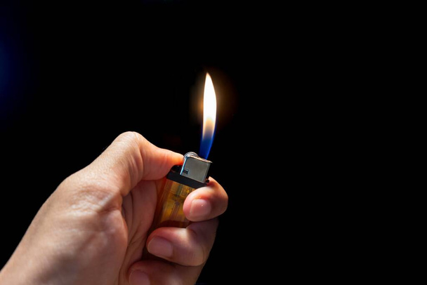 Hand holding a burning lighter isolated on dark background. Cigarette lighter in hand. - Photo, Image