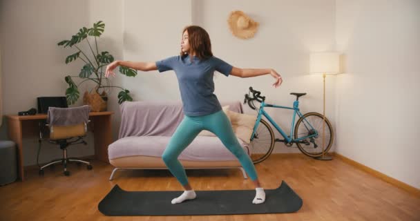 Латинська жінка балансує йога асан вдома. Концентрована струнка іспаномовна жінка тренується стоячи на килимку у вітальні. Змішана расова толерантність - Кадри, відео