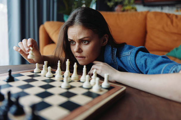 Genç bir kadın, arka planda kanepesi olan rahat bir oturma odasında stratejik bir satranç oynuyor. - Fotoğraf, Görsel