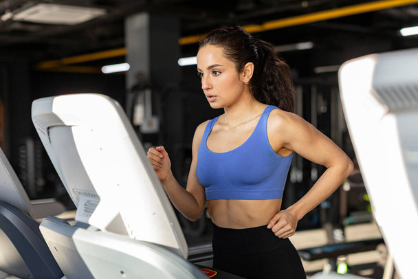 Орієнтована фітнес-леді робить кардіо вправи в спортзалі, бігає на біговій доріжці, леді в спортивному одязі в клубі здоров'я вранці - Фото, зображення