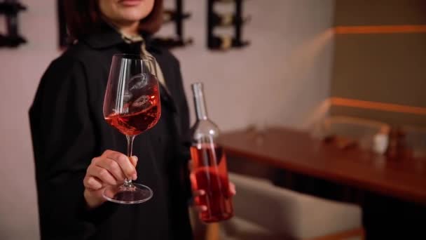Detailní záběr ženy, jak ochutnává červené víno ve vinném sklepě. Šťastná mladá žena vybírá a kupuje víno v soukromém vinařství. Žena sommelier drží víno sklenice a láhev - Záběry, video