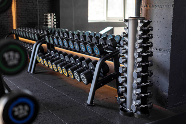 Stand with various dumbbells, weight training equipment, black dumbbell set on rack in modern sport fitness center - Photo, Image