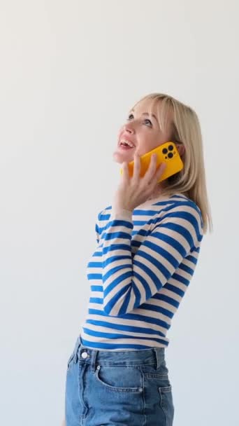Χαρούμενη και φιλική Καυκάσια γυναίκα που χρησιμοποιεί το τηλέφωνο για κλήση και μιλάει σε λευκό φόντο. Απομακρυσμένη συνομιλία και επικοινωνία. Κάθετη βίντεο. - Πλάνα, βίντεο