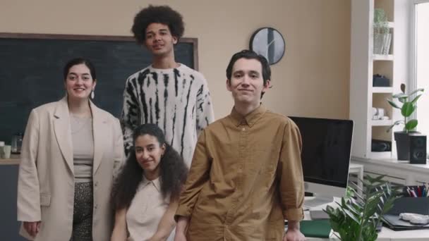 Medium muotokuva nuori hymyilevä monirotuinen ohjelmoijat joukkue neljä poseeraa kameran nykyaikainen toimisto liitutaulu seinällä taustalla - Materiaali, video