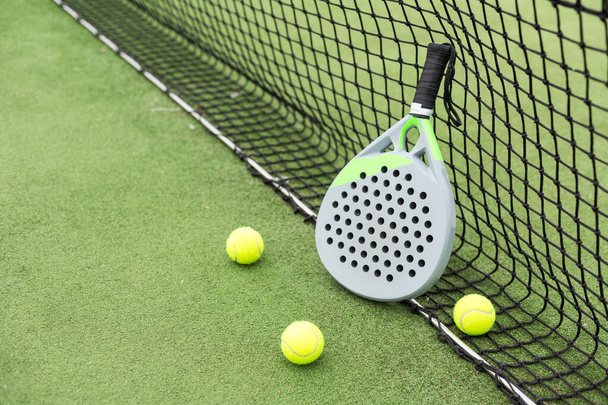 Bolas amarelas em relva perto padel raquete de tênis atrás da rede na quadra verde ao ar livre com iluminação natural. Raquete é um jogo de raquete. Conceito de esporte profissional com espaço de cópia. Foto de alta qualidade - Foto, Imagem