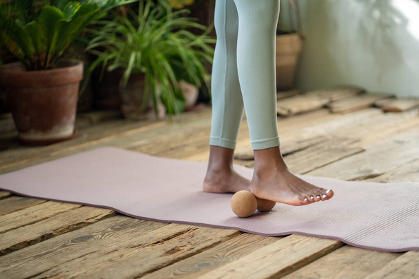 Yoga minderinde bacaklar yuvarlanan fitness topu. Siyahi kadın özbakımı, miyofasyal masaj topu, yuvarlanan ayak, gevşeme ve kan dolaşımını iyileştirme ile çalışır. Sağlıklı yaşam tarzı için spor aletleri. - Fotoğraf, Görsel
