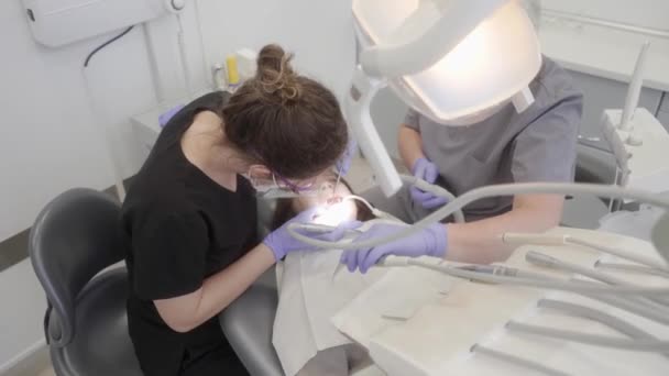 Léčba caries u dítěte v pediatrické stomatologii. Zubař a asistent společně provedou lékařskou proceduru pomocí vrtačky, zubního zrcátka, pumpy na sliny a orálního zavlažovače. - Záběry, video