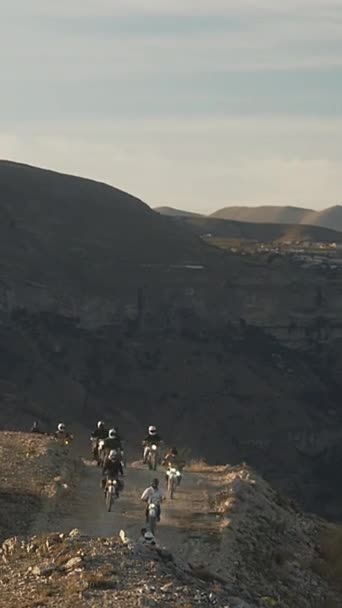 Ta pionowa rama uchwyciła grupę motocyklistów jadących w formacji wzdłuż wąskiej ścieżki brudu wyrzeźbionej w zboczu góry. Jeźdźcy, ubrani w sprzęt ochronny z reflektorami oświetlającymi - Materiał filmowy, wideo