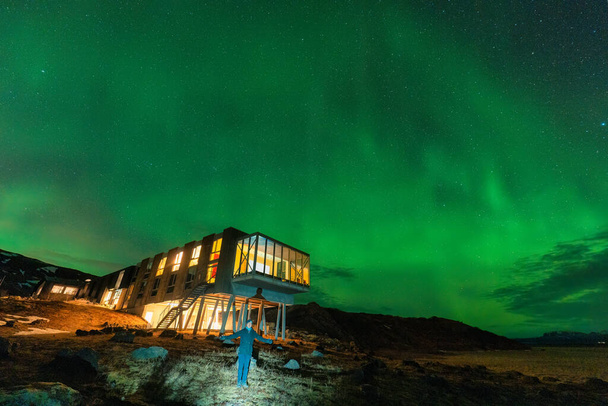 Прекрасний мальовничий вид на боаліс Аврори, північне сяйво, що світиться над розкішним готелем і чоловічим туристом, насолоджуючись на горі Хенгілл взимку в Несав'єрі, Ісландія - Фото, зображення