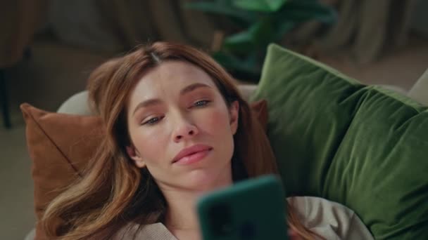 Woman reading cellphone news feed lying comfortable couch close up. Relaxed attractive girl looking smartphone screen relaxing home alone. Calm bored lady resting in cozy apartment with mobile phone. - Footage, Video