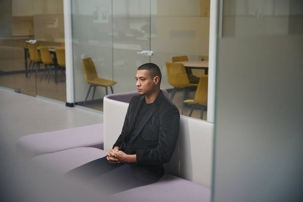 Продуманий афроамериканський хлопець сидить на затишному дивані в сучасному офісі, чекаючи на співбесіду - Фото, зображення