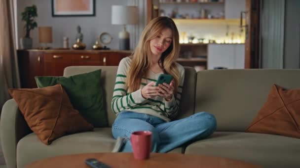 Calm woman chatting cellphone on cozy home couch. Relaxed young lady making online order using smartphone application in living room. Carefree freelancer browsing internet website at mobile phone. - Footage, Video