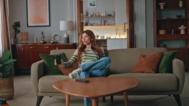 Bored woman looking mobile phone relaxing on comfortable sofa. Tired housewife putting smartphone on couch uninterested news feed. Attractive young girl resting at home weekend alone feeling boredom. - Footage, Video