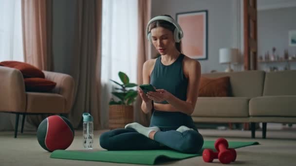 Yoga yapan kadın evde nilüfer nilüfer pozisyonu için müzik aleti açıyor. İnternette meditasyon dinleyen kulaklıklı sakin bir kız spor minderinde oturuyor. Güzel bayan sabah zihin dengesi hisseder.. - Video, Çekim